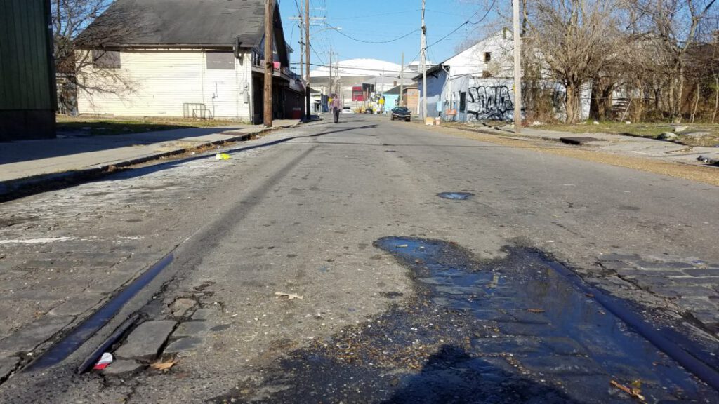 Erosion uncovers old cobblestone and streetcar tracks in Central City. Superdome in background.