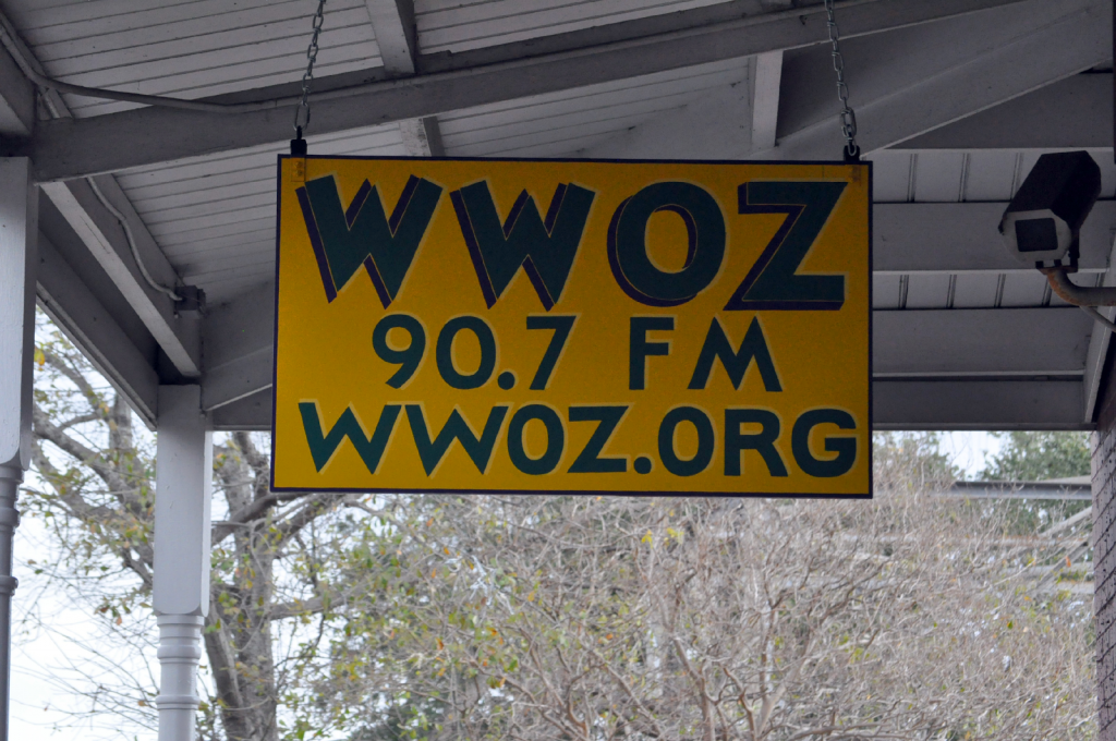 Photo Credit: ACloserWalkNola.com. This bright yellow sign hangs outside WWOZ’s French Market station.